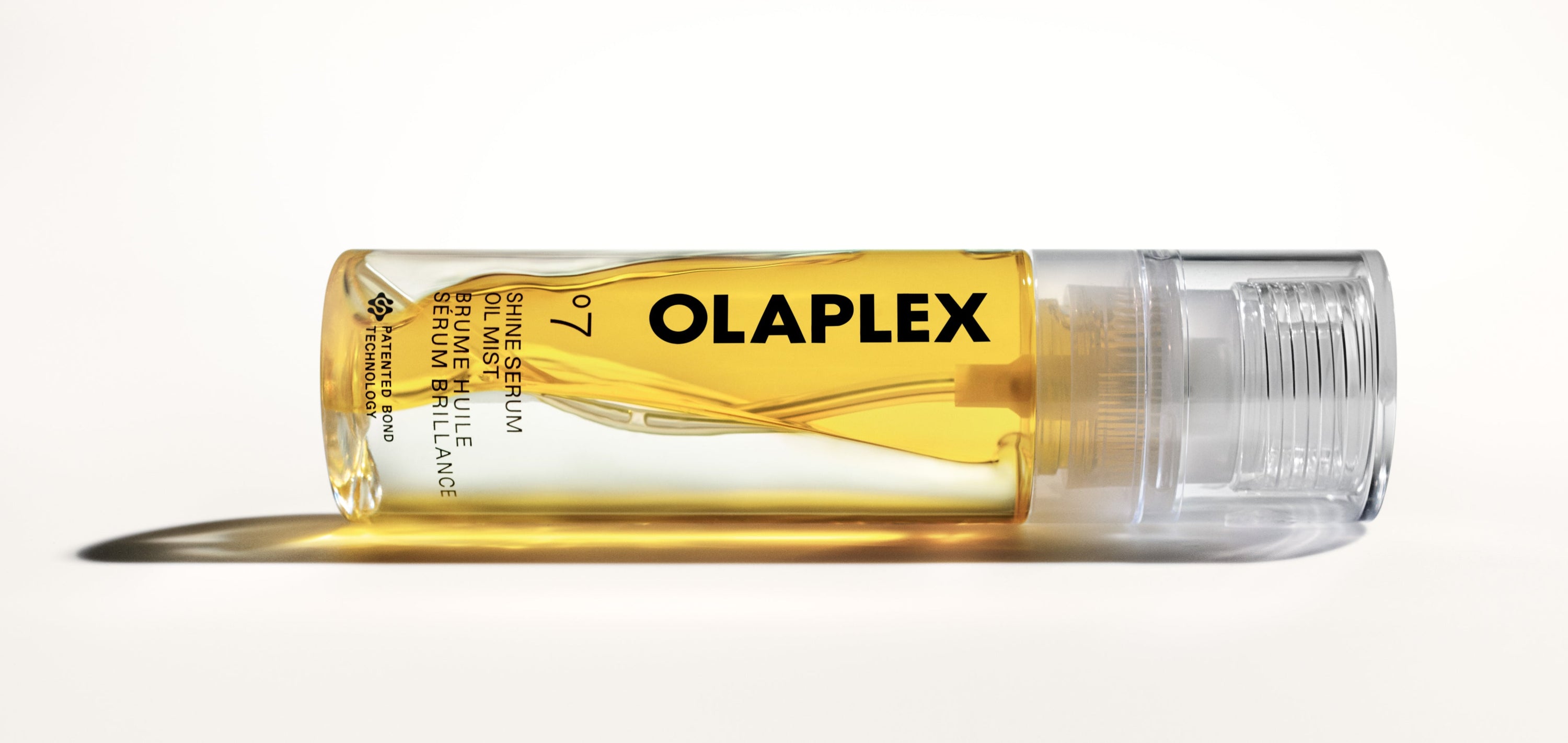 A bottle of °.7 Shine Serum Oil Mist lying horizontally with oil flowing from it
