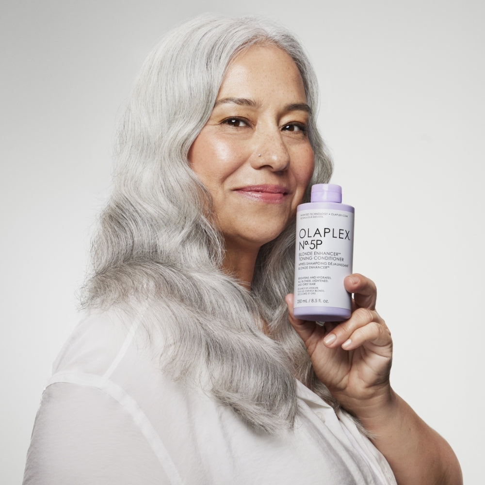 Woman with gray hair holding OLAPLEX No.5P Blonde Enhancer™ Toning Conditioner