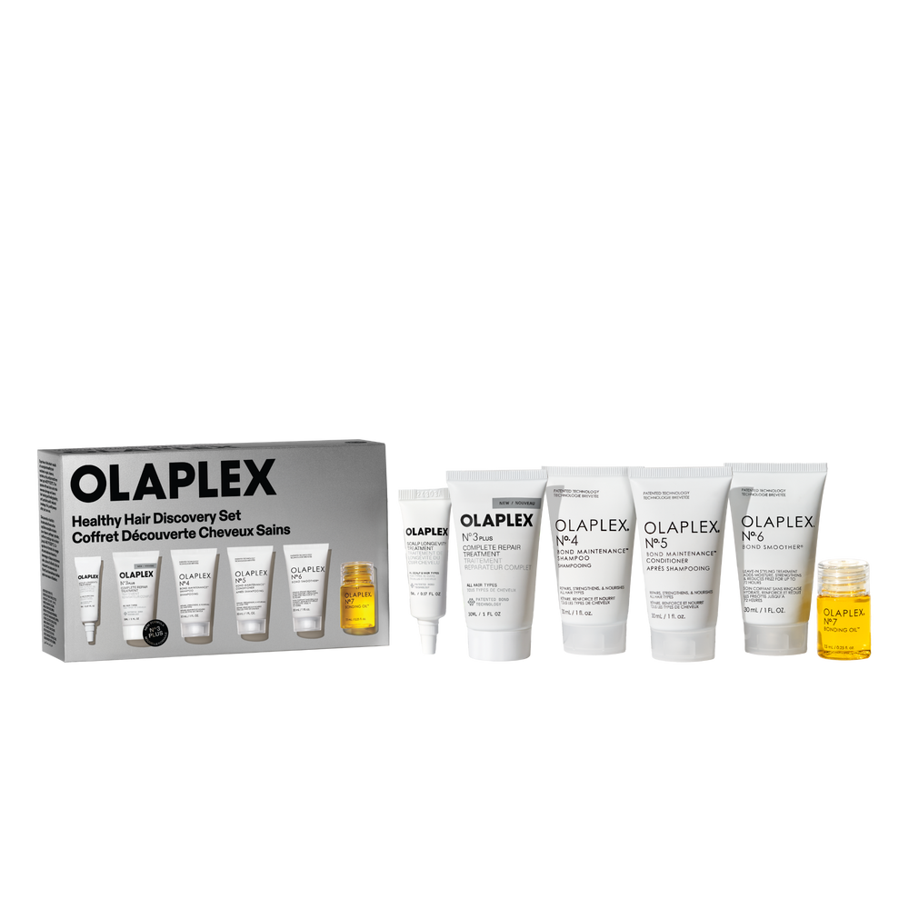 Une photo de produit de l'Olaplex Healthy Hair Discovery Set d'Olaplex, sur un fond transparent à damier. À gauche se trouve la boîte du produit, et à droite se trouvent cinq tubes blancs de taille voyage (N°.3, N°.4, N°.5, N°.6 et un tube plus petit) à côté d’une petite bouteille transparente de N°.7 BONDING OIL remplie d’un liquide jaune. - main view