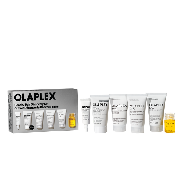 Une photo de produit de l'Olaplex Healthy Hair Discovery Set d'Olaplex, sur un fond transparent à damier. À gauche se trouve la boîte du produit, et à droite se trouvent cinq tubes blancs de taille voyage (N°.3, N°.4, N°.5, N°.6 et un tube plus petit) à côté d’une petite bouteille transparente de N°.7 BONDING OIL remplie d’un liquide jaune. - main view