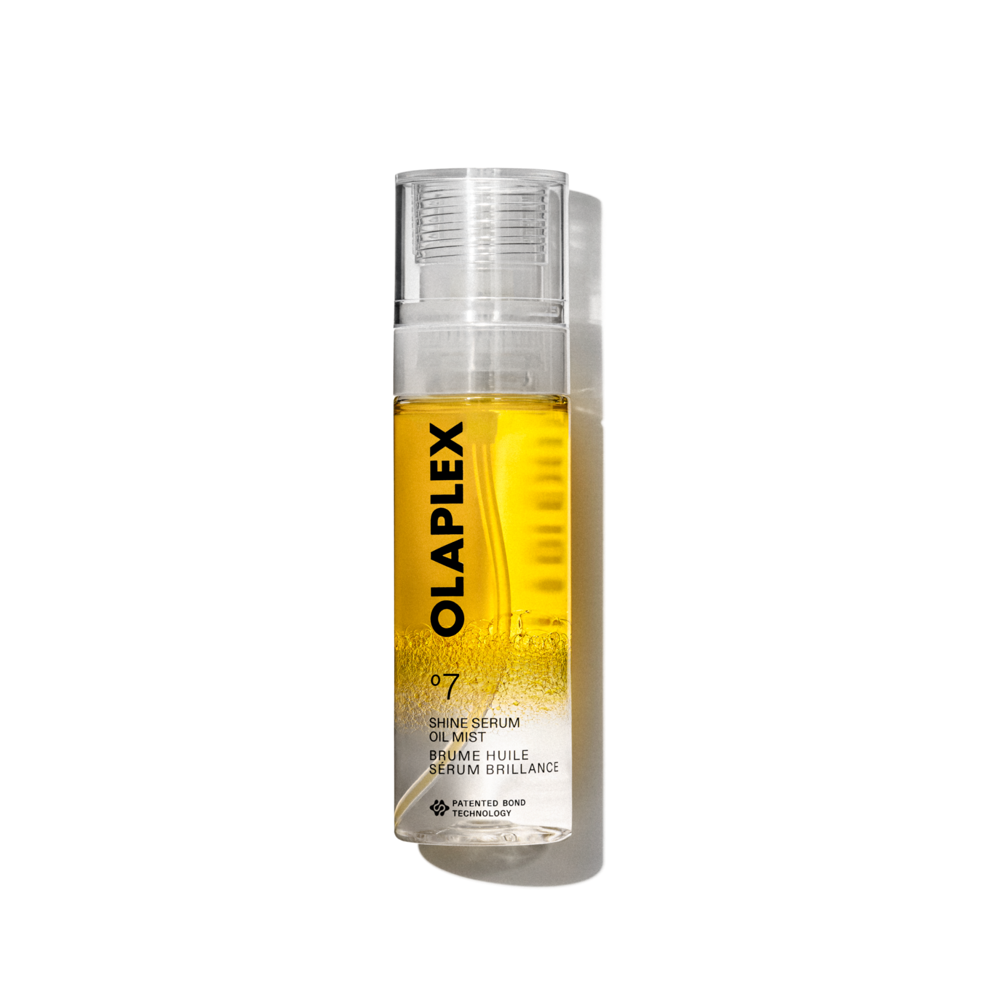 Photo du produit Olaplex No. 7 Shine Serum Oil Mist dans un flacon pulvérisateur transparent de 80 ml. La bouteille présente un liquide jaune vif visible à l'intérieur, un capuchon transparent et une étiquette blanche propre au bas avec un texte noir affichant le nom du produit, les détails et la signature "No. 7 " logo. La bouteille est isolée sur un fond quadrillé transparent.