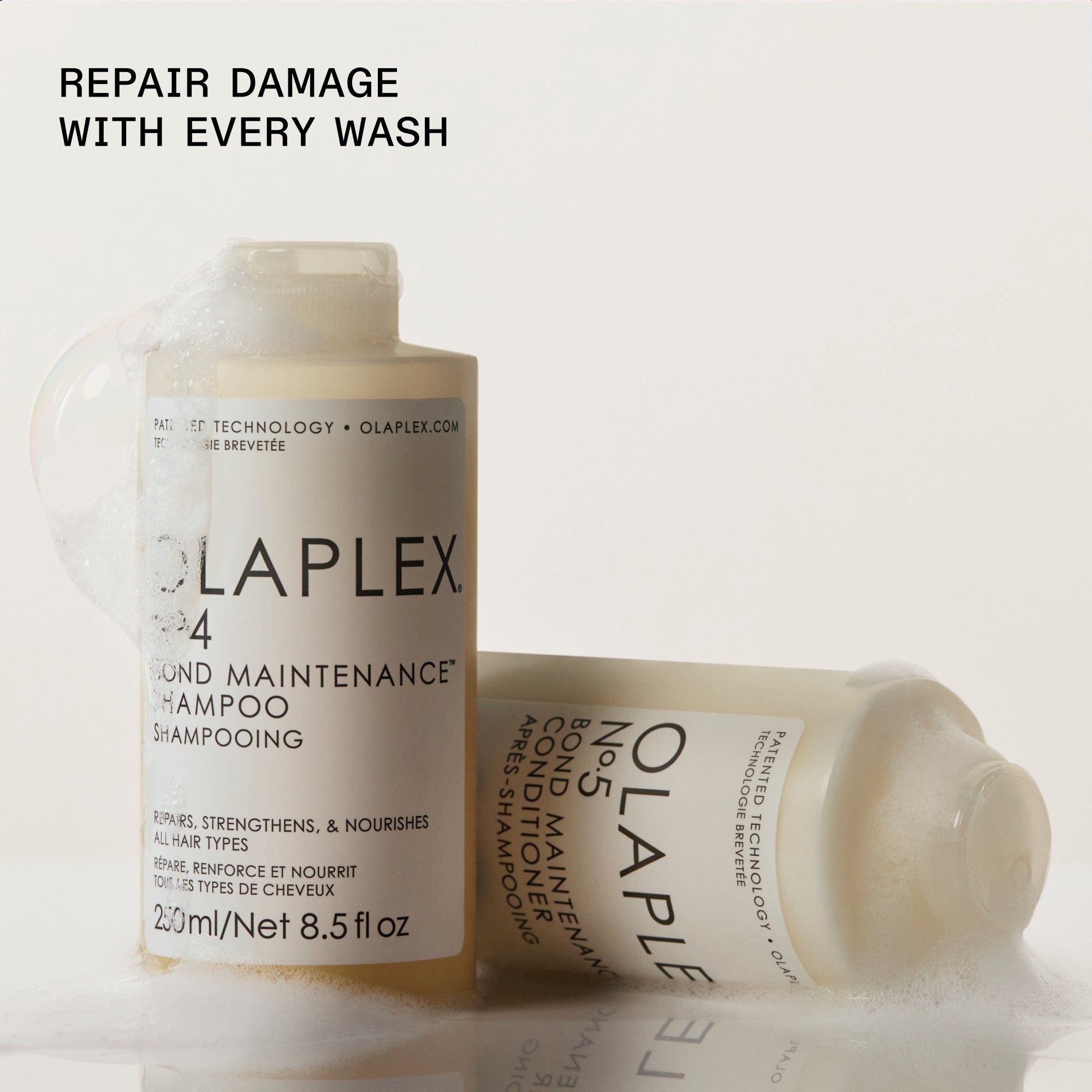 Flacons de shampoing et de revitalisant Olaplex positionnés sur un fond clair. À gauche, une bouteille debout de « OLAPLEX N°.4 BOND MAINTENANCE SHAMPOO » est représentée, tandis qu'une bouteille de « OLAPLEX N°.5 BOND MAINTENANCE CONDITIONER » repose horizontalement sur le côté droit. Le texte noir en gras dans le coin supérieur gauche indique : « Réparez les dommages avec chaque lavage. »