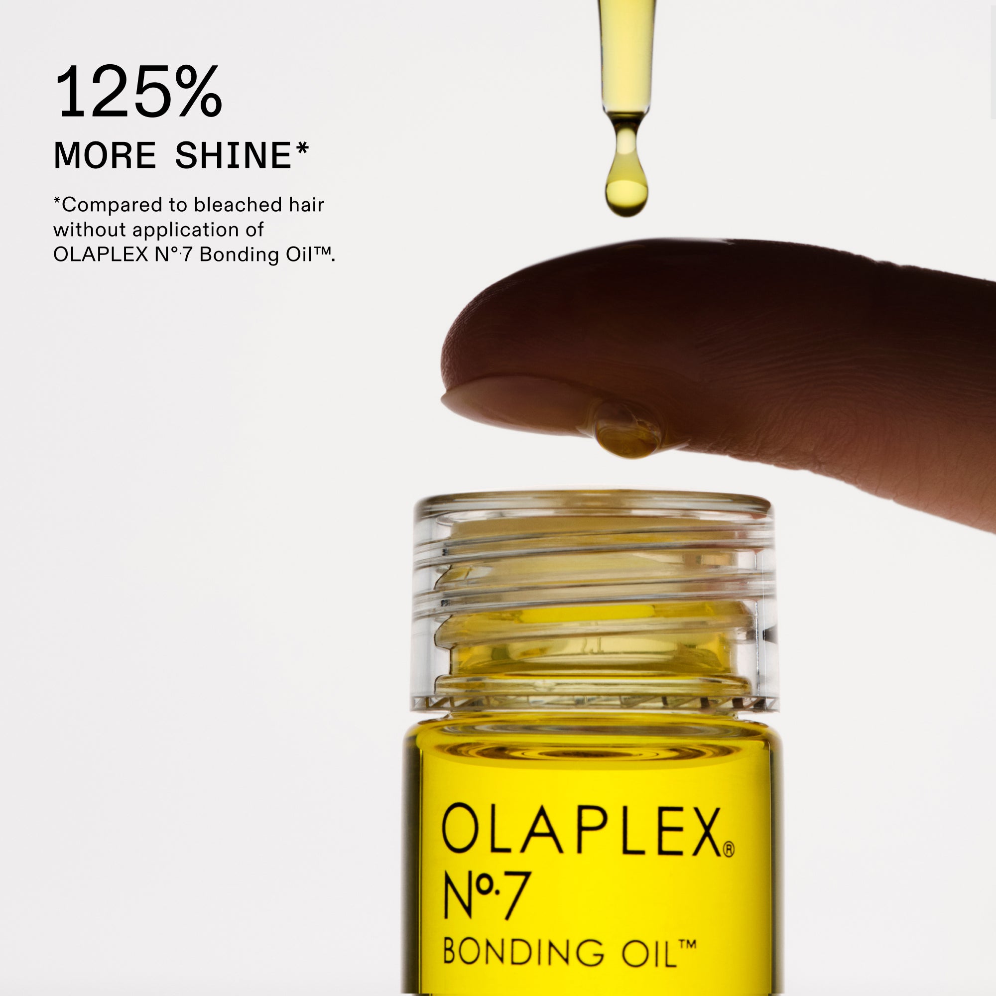Une mise en page présentant les caractéristiques d'un produit Olaplex sur un fond blanc uni. À gauche, un grand texte noir en gras indique « 125 % PLUS DE BRILLANCE* », avec une note de bas de page plus petite en dessous. À droite, un gros plan montre une goutte d'huile jaune tombant d'un compte-gouttes transparent sur le bout d'un doigt. Juste en dessous se trouve un flacon en verre transparent d'OLAPLEX N°.7 BONDING OIL™, rempli d'un liquide d'un jaune éclatant.